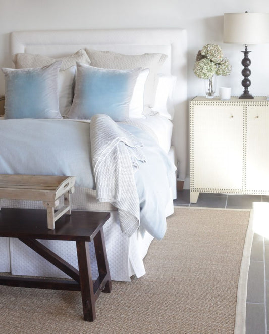 Nicely designed bed in pastel shades next to a night stand with white flowers, by Brooke & Steve Giannetti
