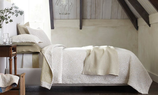 A well-dressed bed in shades of white and linen sits under a vaulted ceiling