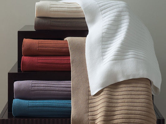 A stack of richly colored knit ribbed throw blankets
