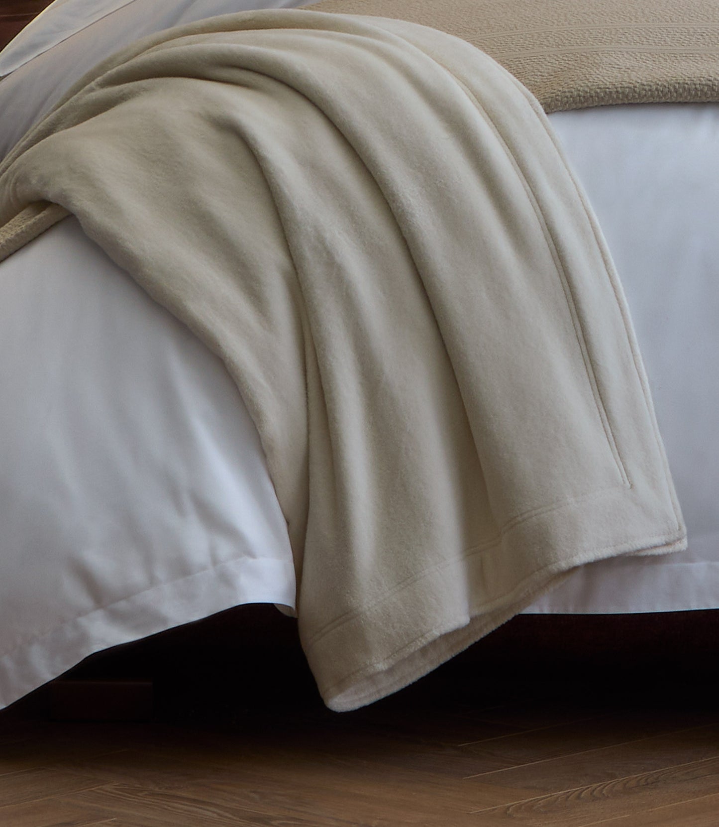 All Seasons Cotton Blanket laid over the corner of a white bed
