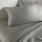 Clara Sateen Sheet Set and Pillowcases in Light Gray on bed 