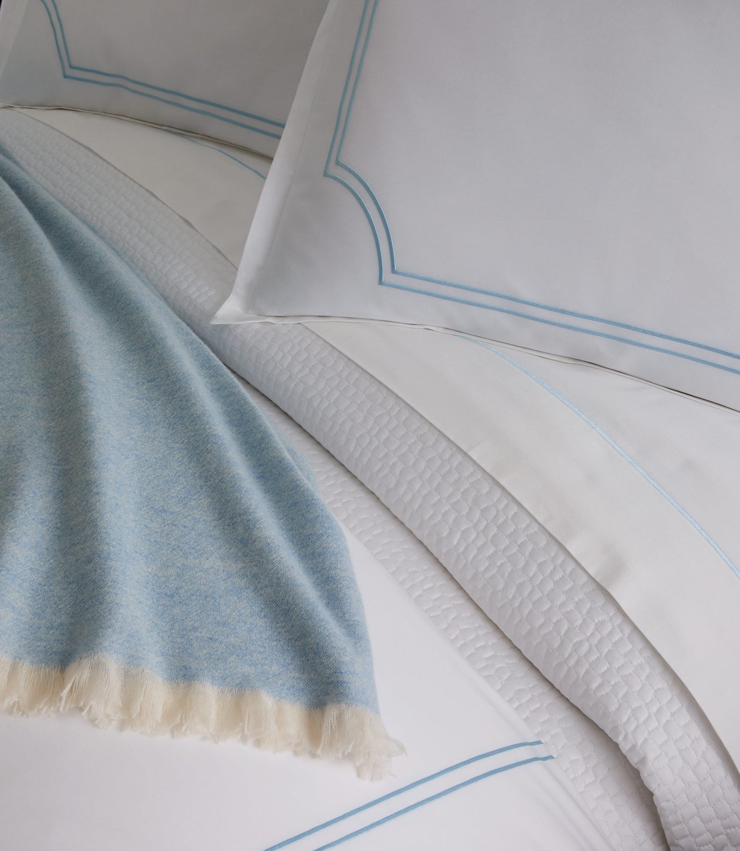 Close-up of satin stitch trim on the Deco Classic Embroidered Duvet Set in Sky and a light blue blanket.