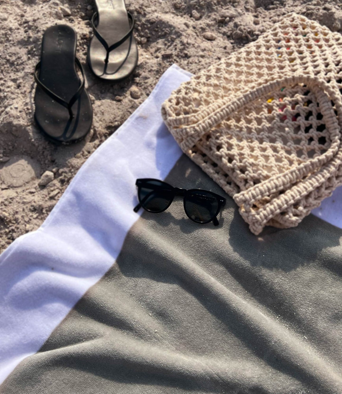 Flatlay of a Soleil Beach Towel White Trim with sunglasses, sandals and a straw tote
