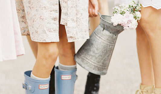 Little girl in rain boots carrying a watering can with flowers in it