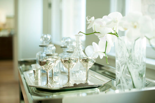 Fine drinkware sits on a silver tray next to a vase of white orchids