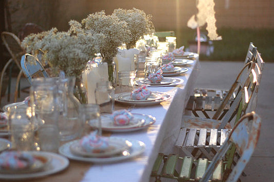 A rustic outdoor table with floral arrangements, candles, and weathered folding chairs