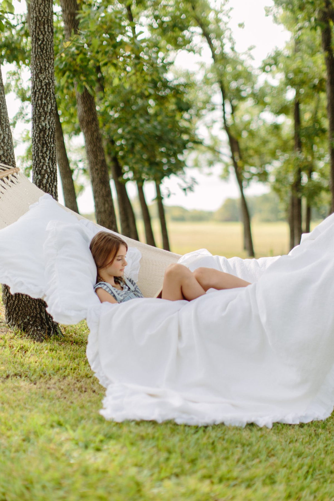 Young girl reading on a hammock with a ruffled white duvet