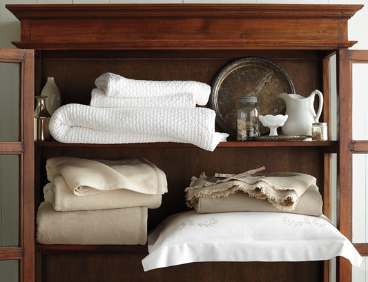 A selection of luxury bedding linens folded and shelved with other household decor items