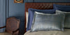Close-up of blue and navy shams layered on a bed in a moody, elegant room.