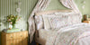 Chloe duvet and sheet set, layered with white shams against a green and white striped wall.
