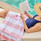 Woman with an Aegean Stripe Beach Towel over her lap while reading by the pool, Coral