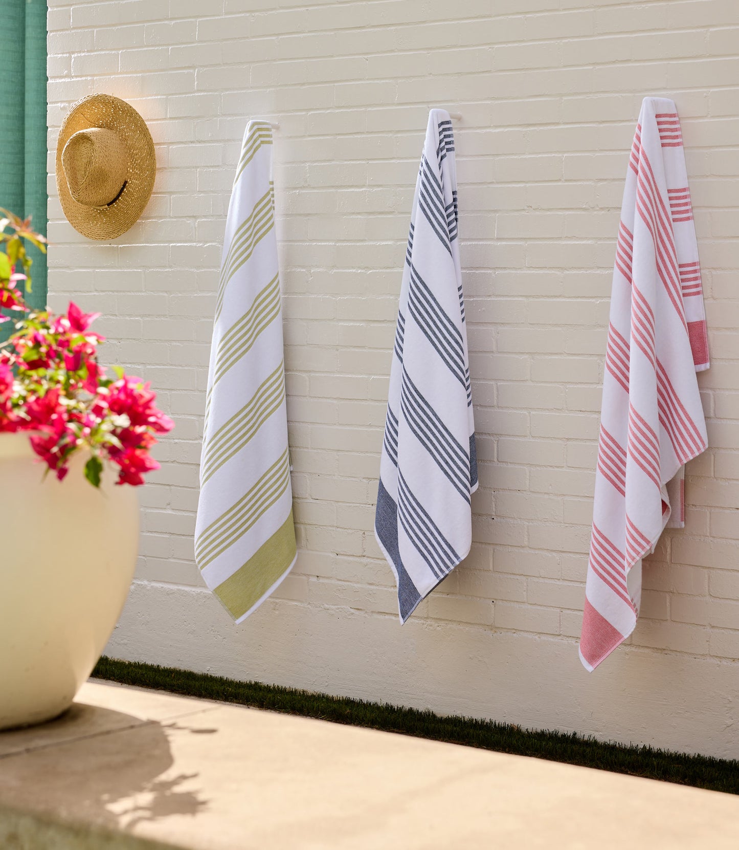 Three Aegean Beach Towels hanging on a wall next to a potted plant, Lime Navy Coral