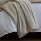 All Seasons Cotton Blanket laid over the corner of a white bed