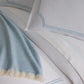 Close-up of satin stitch trim on the Deco Classic Embroidered Duvet Set in Sky and a light blue blanket.