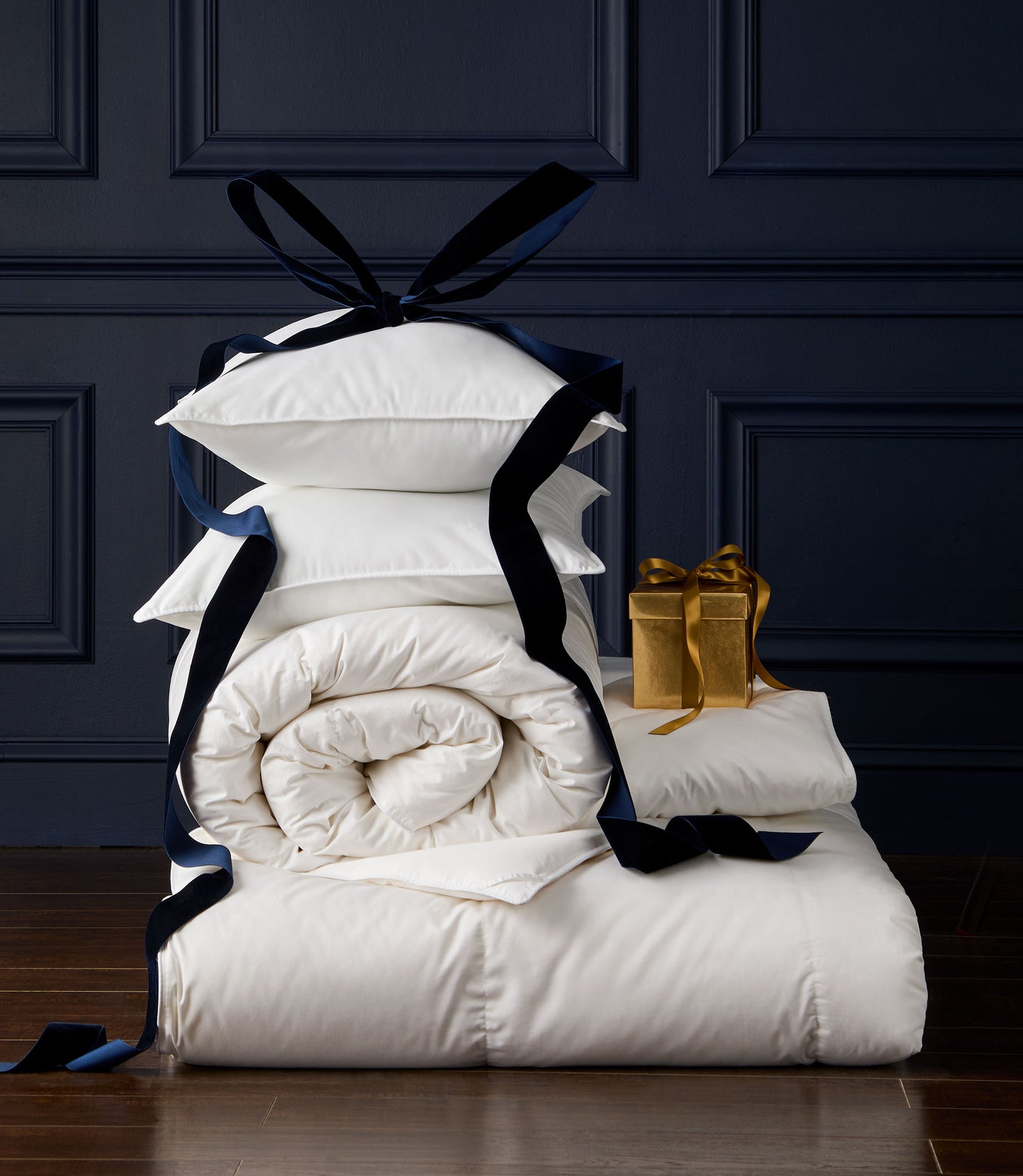 Stack of Down Alternative Duvet and Pillows with navy ribbons against a dark paneled wall
