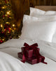White monogrammed bedding with stacked maroon gift boxes and a dark red ribbon on a bed.