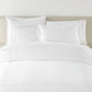 Filigree Duvet Set arranged on a bed against a light beige headboard, White