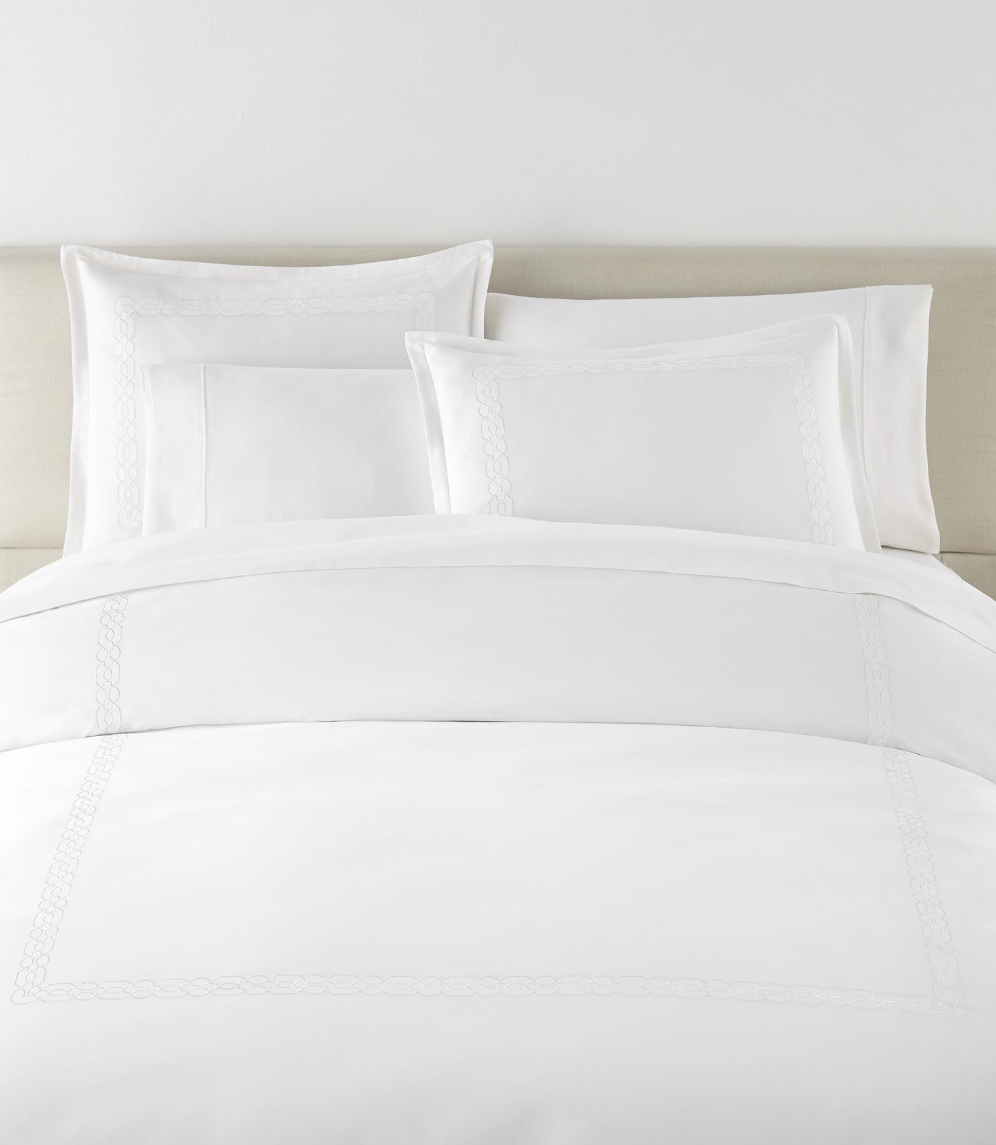 Filigree Duvet Set arranged on a bed against a light beige headboard, White