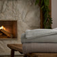 Hampton Throw Blankets stacked on top a wooden stool next to a fireplace, Gray, Mushroom