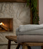 Hampton Throw Blankets stacked on top a wooden stool next to a fireplace, Gray, Mushroom