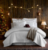 A neatly made bed with white bedding and pillows, a lit Christmas tree, bedside lamps, and a draped throw blanket.