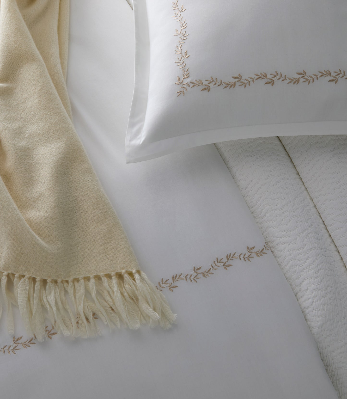 Close up of vine detailing on the Ivy Classic Embroidered Duvet Set in Linen with a cream colored throw blanket.