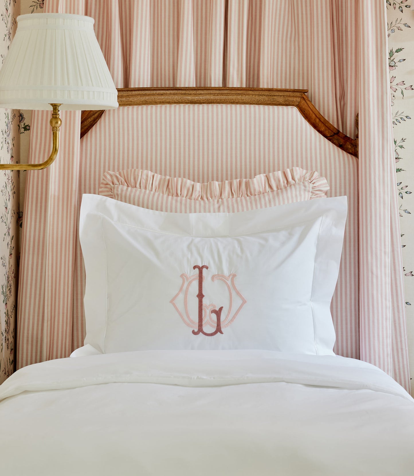Soprano Sateen Sham in White featuring a monogram, displayed on a bed with a light pink striped headboard.