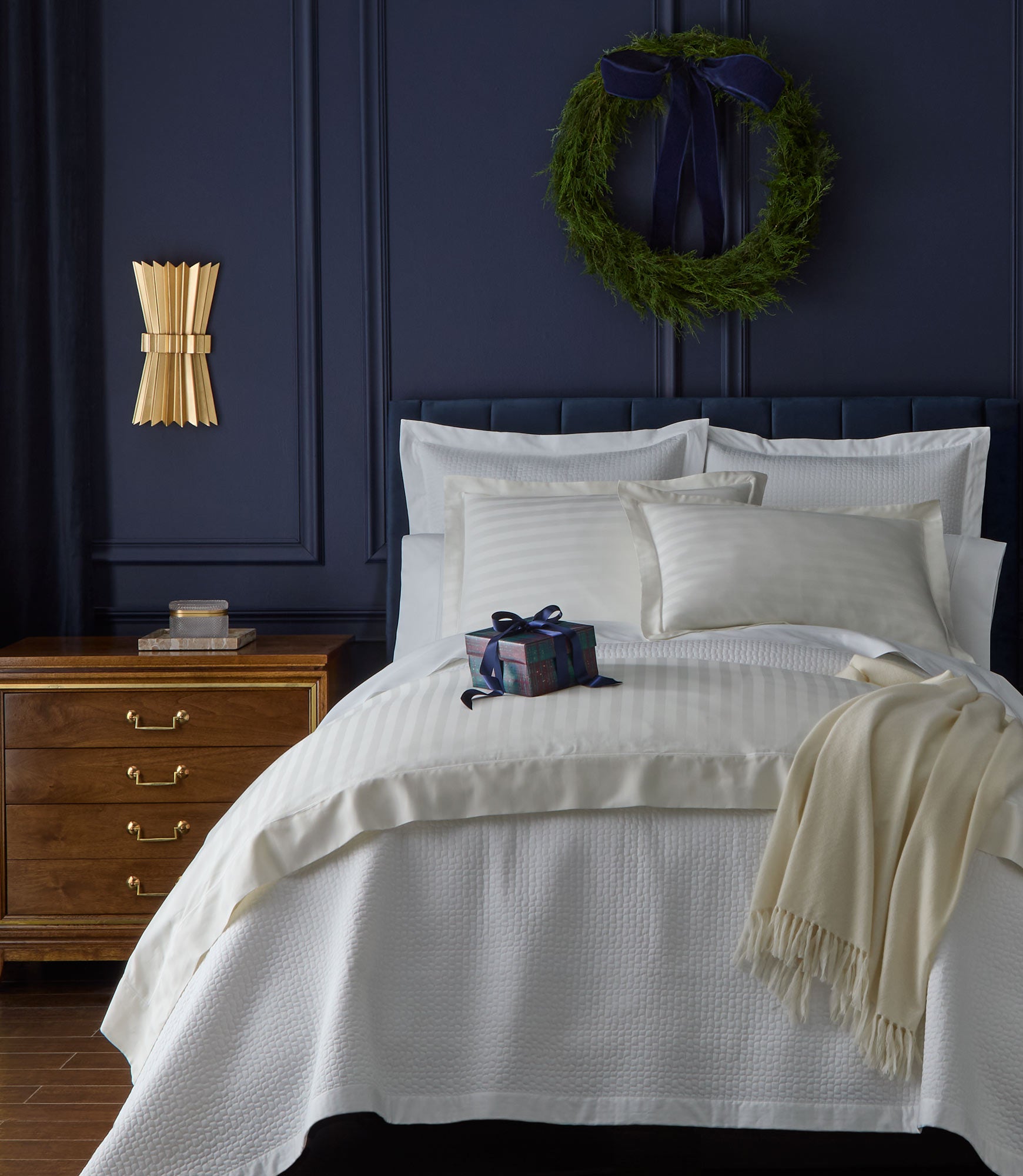 Neatly made bed with Soprano Striped Duvet Set and a decorative wreath on a navy blue wall.