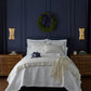 Neatly made bed with Hamilton Coverlet and Shams in a bedroom with dark blue walls and gold accents.