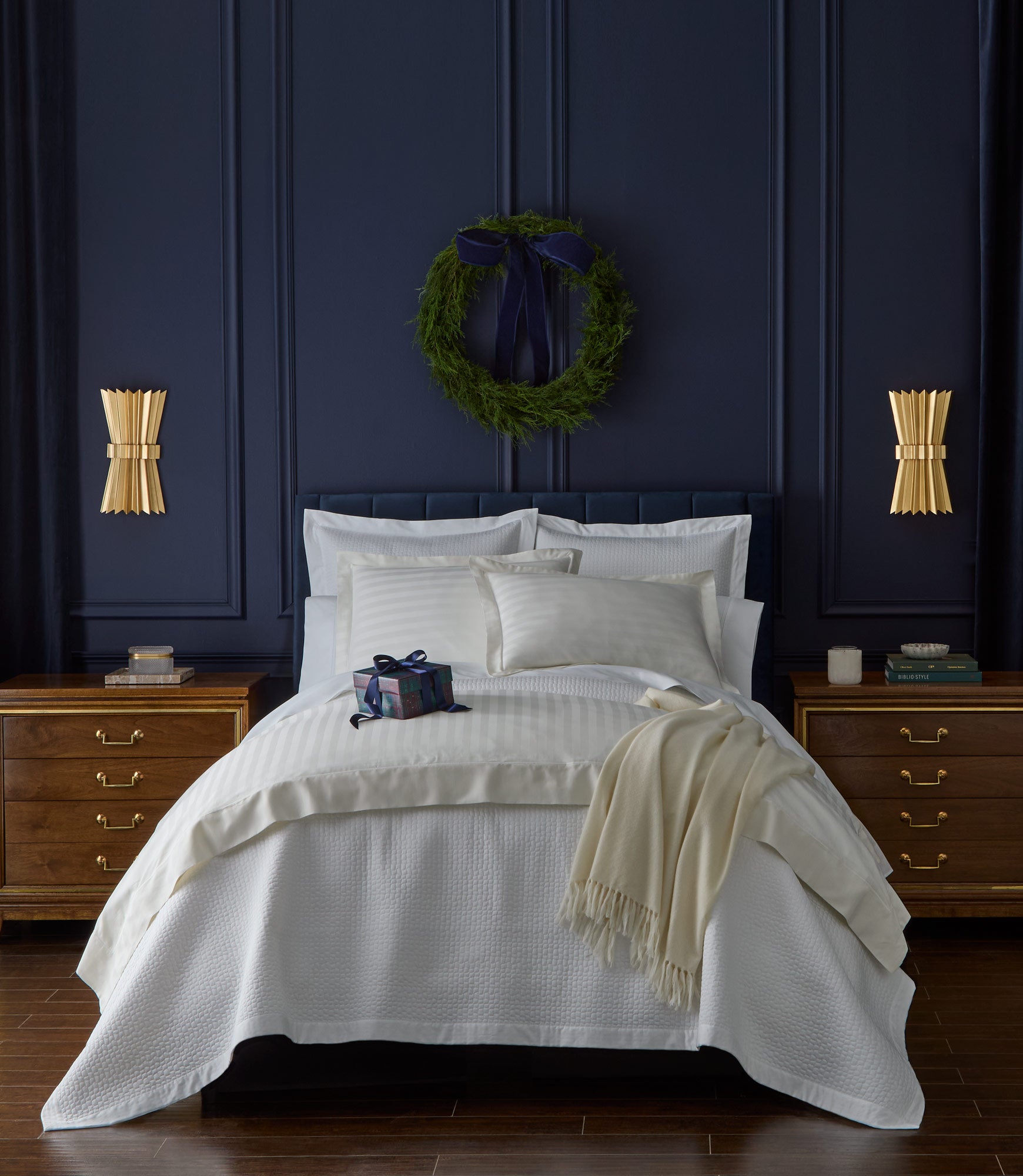Neatly made bed with Hamilton Coverlet and Shams in a bedroom with dark blue walls and gold accents.