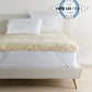 Wool mattress topper with elastic straps on bed with Oprah Daily Sleep O-Wards logo in the corner.