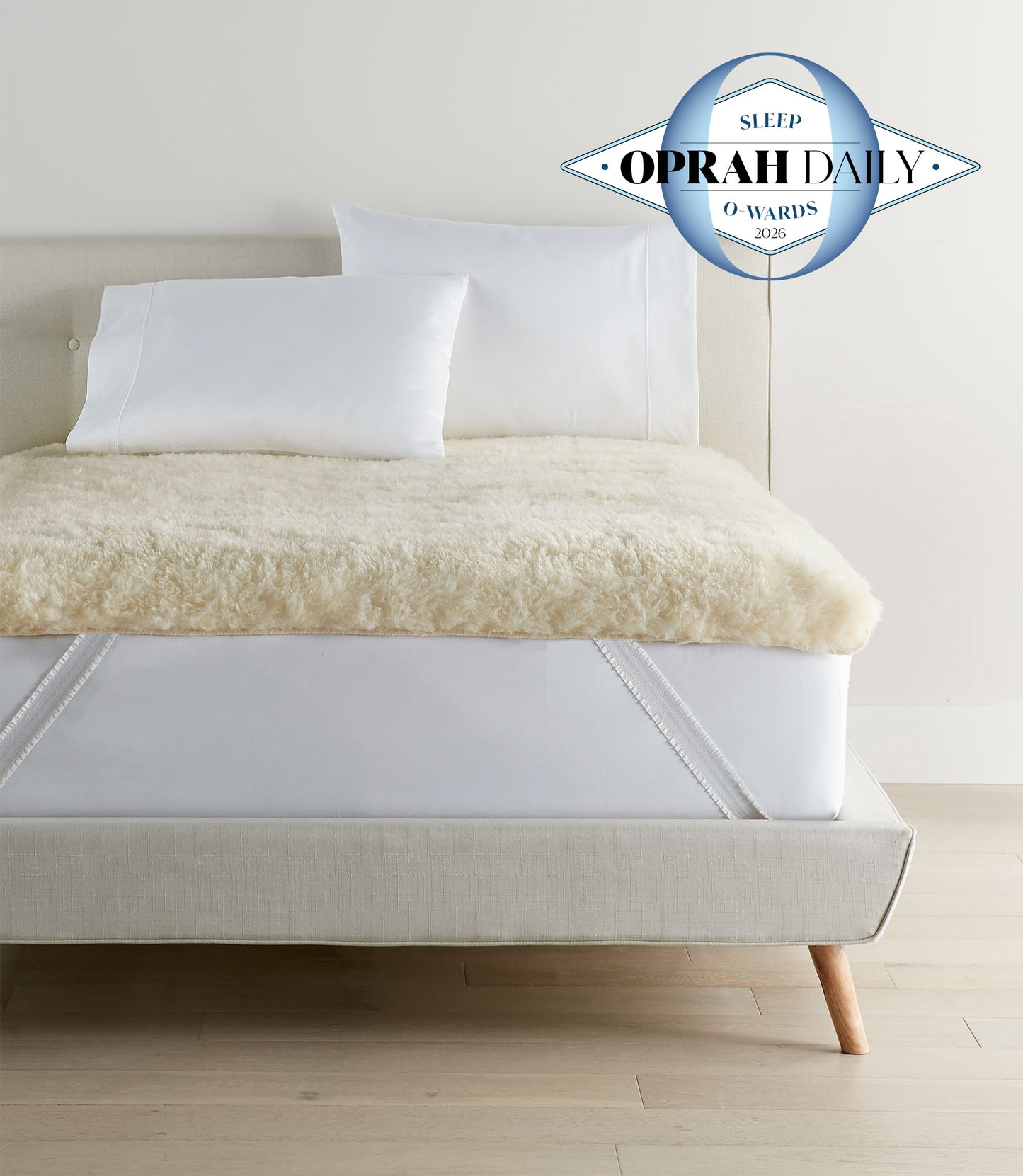 Wool mattress topper with elastic straps on bed with Oprah Daily Sleep O-Wards logo in the corner.