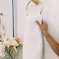 Jubilee Textured Bath Towel hanging on a gold towel ring, White