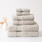 Stack of six plush, beige Turkish cotton towels with a sophisticated border, neatly folded on a white marble surface.